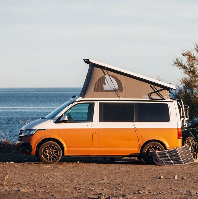 An orange and white campervan with its pop-top roof raised, parked above the sea