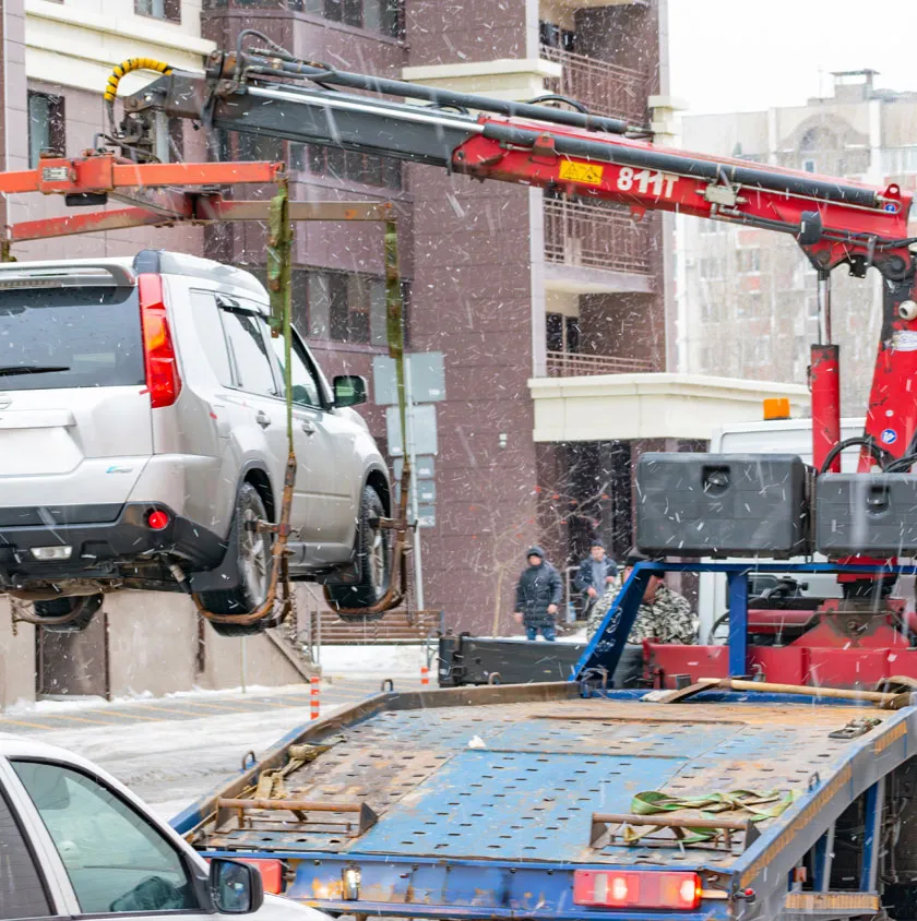 A silver car being lifted onto the back of a recovery truck in the snow