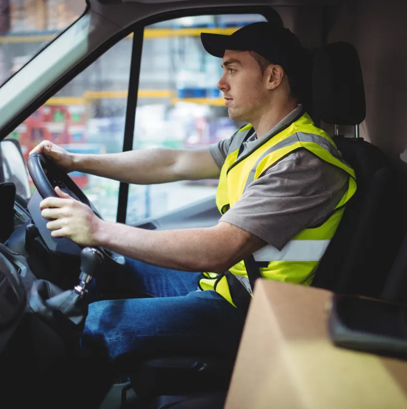 A courier in a hi-vis vest at the wheel of a van with a parcel on the passenger seat