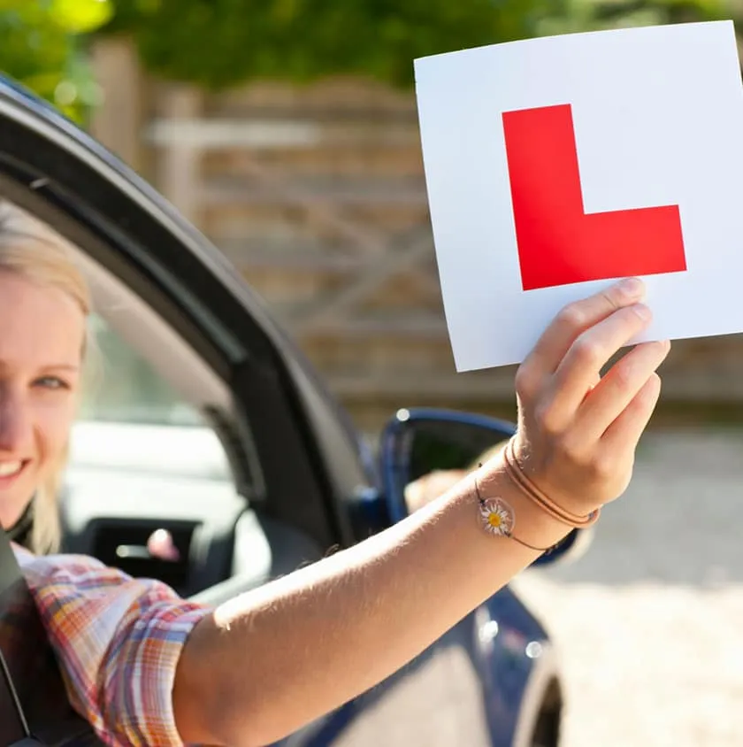 A learner driver holding a red L plate out of a car window