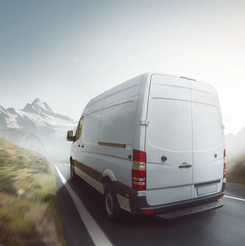 A white panel van on an open road with mountains behind it